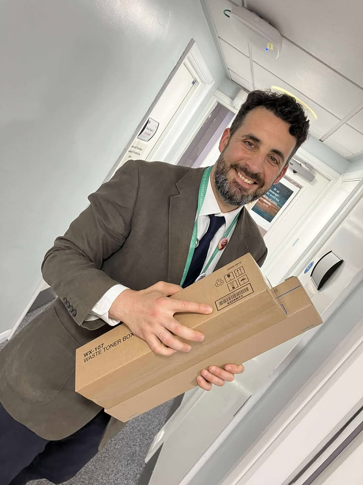Andrew Poppa, a Green Champion for the Trust, stands in a corridor holding some printer cartridges